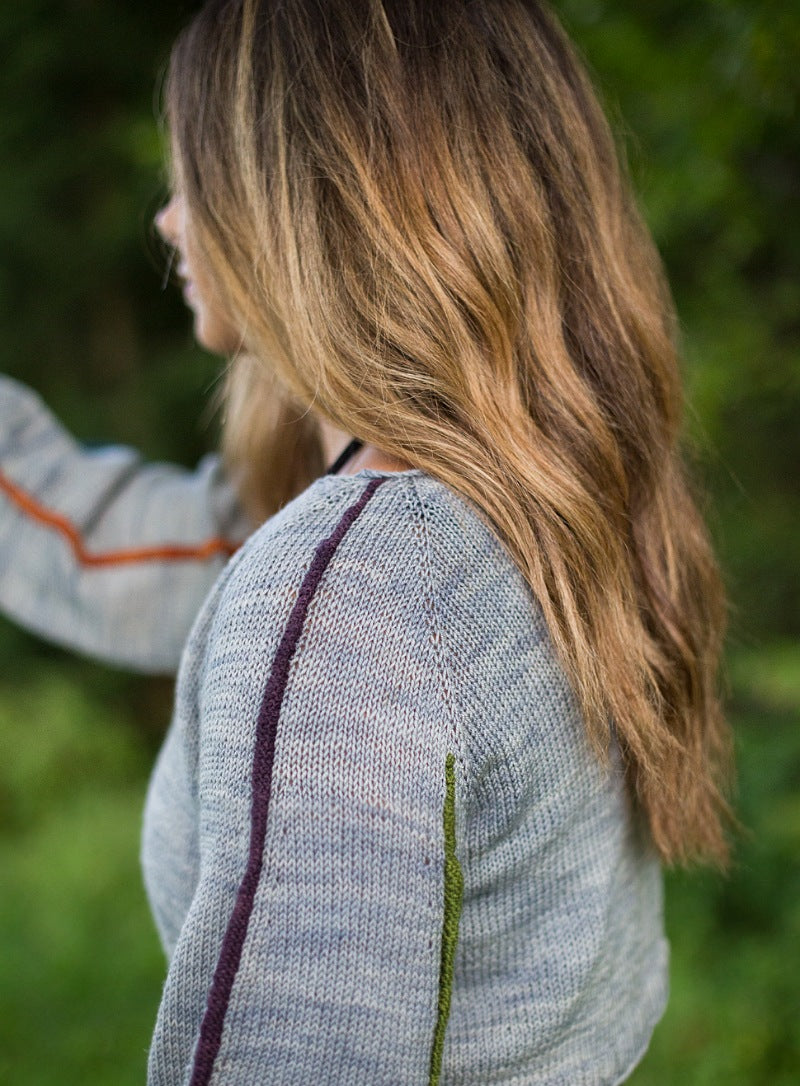 blonde woman facing away in a grey knit sweater with stripes on the sleeves