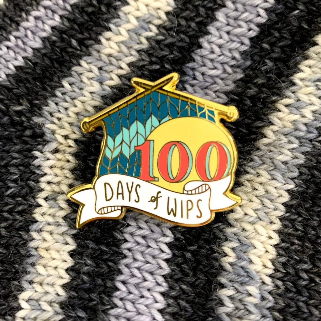 Striped knit backdrop with an enamel pin of striped teal knitting that reads 100 days of WIPs