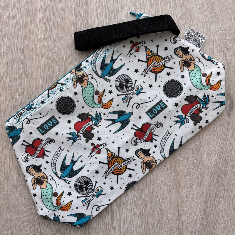 White pouch with tattoo-style design on a wooden surface