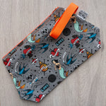 Grey pouch with tattoo-themed design and orange handle on a wooden surface