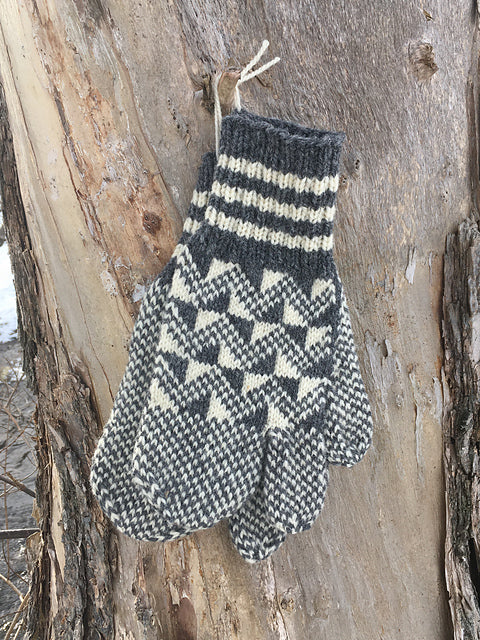 a pair of grey and cream colourwork mittens hanging on a tree
