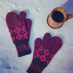 A pair of fuscia and navy knit trigger finger mittens sitting in the snow beside a handmade clay coffee cup full of coffee