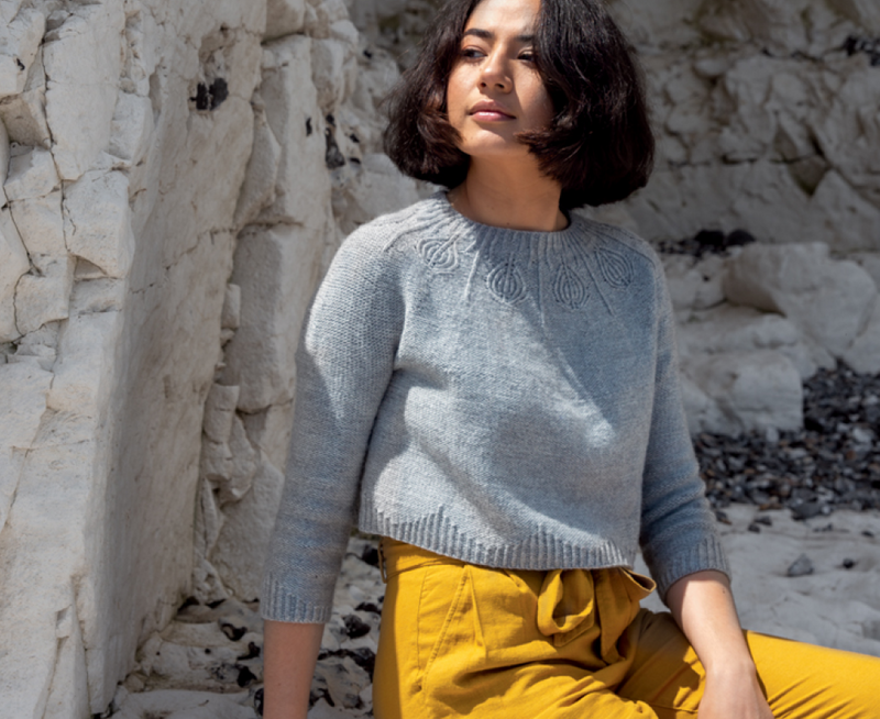 woman sitting by cliffs wearing a light grey knit sweater with a patterned yoke