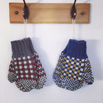 a pair of grey, burgundy, and cream colourwork knit mittens and blue, mustard and cream colour work mittens hanging on hooks