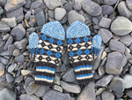 bright blue, cream, and charcoal grey colourwork knit mittens on top of grey beach rocks