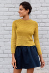 A woman wearing a mustard knit sweater and a navy skirt