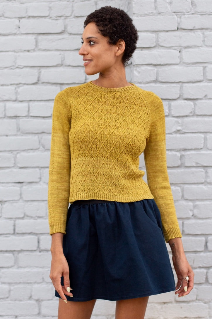 A woman wearing a mustard knit sweater and a navy skirt