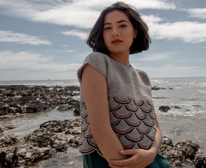 woman standing on a beach wearing a grey knit t-shirt with a black and red shell pattern on the body