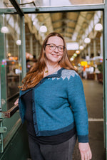 a woman standing in a market wearing a blue knit cardigan with a grey patterened yoke.