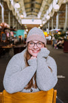 a woman sitting backwards on a chair in a market wearing a grey knit sweater and hat
