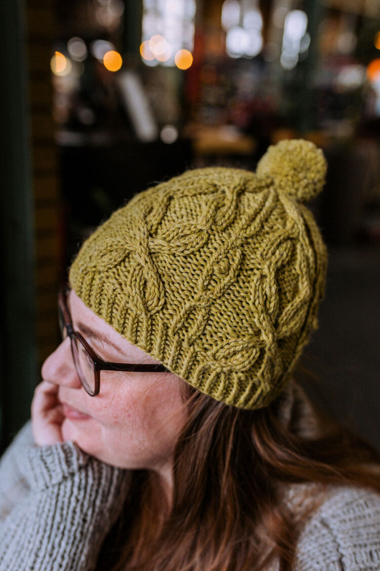 a woman wearing a green hat knit hat with a cable pattern