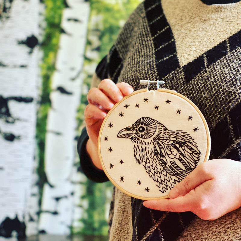 hands holding embroidery of a raven