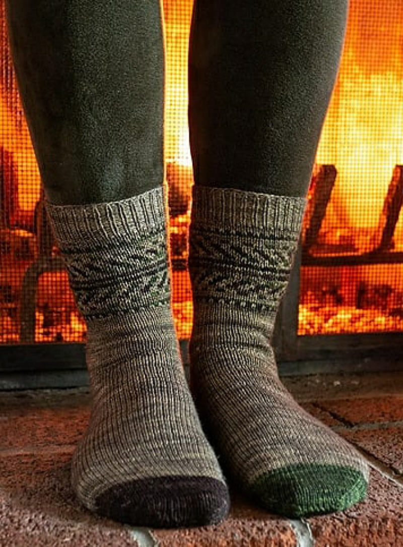 feet standing in front of a fireplace wearing grey knit socks with colourwork