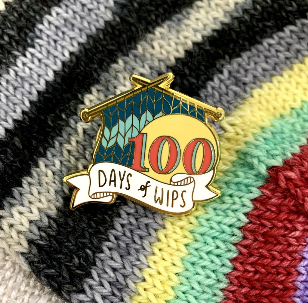 Striped knit backdrop with an enamel pin of striped teal knitting that reads 100 days of WIPs