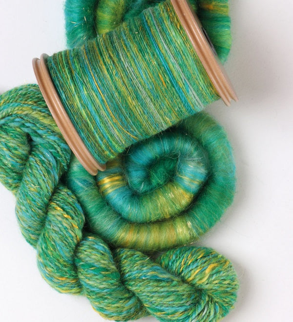 kiwi bobbin holding spun green and yellow fibre, sitting beside a skein of yarn plied from the same fibre and a rolag of roving from the same fibre.