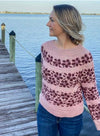 blonde woman standing on a dock wearing a pink knit sweater with deep pink floral stripes
