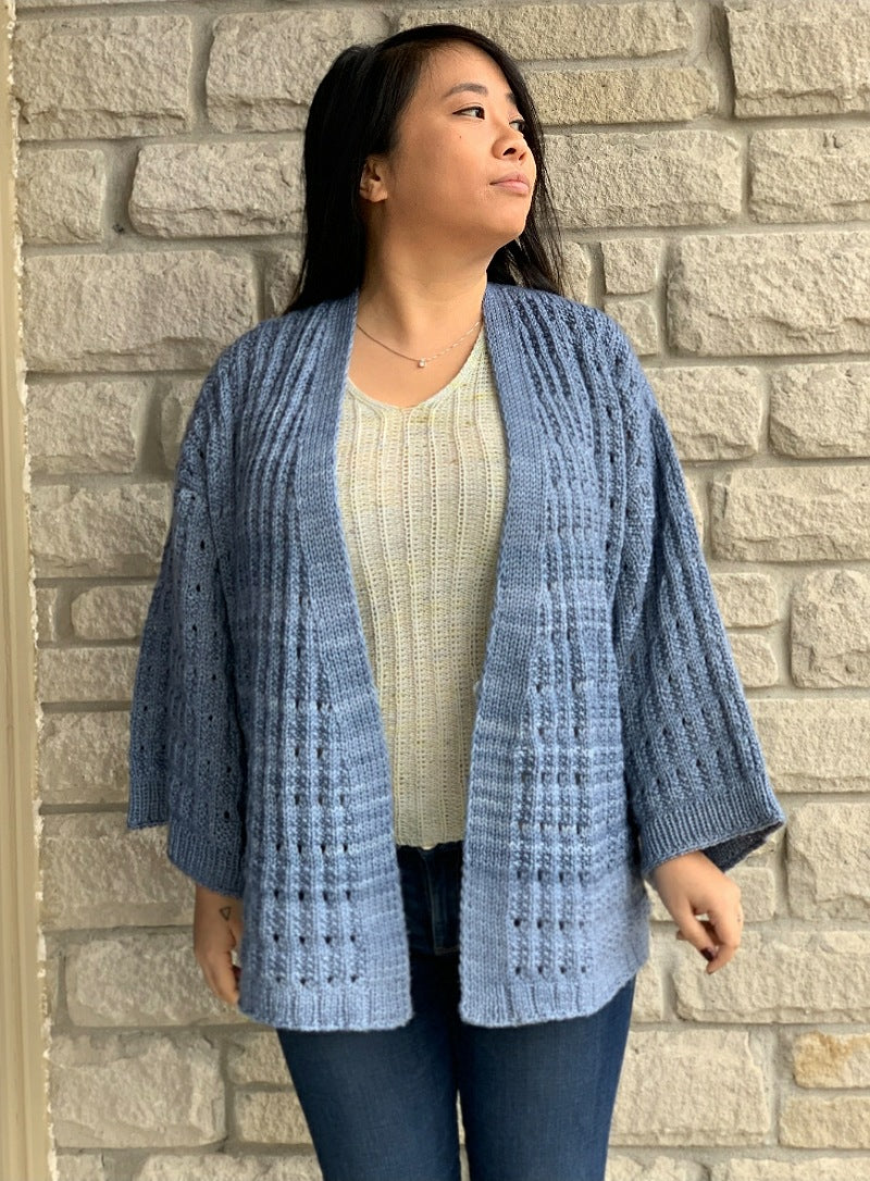 asian woman standing in front of a brick wall wearing a blue knit cardigan
