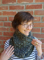 A woman smiling wearing a blue-green knit cowl