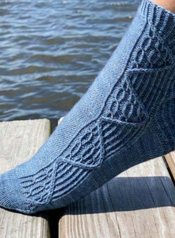 A foot wearing a cable-patterned knit sock in medium blue standing on a dock